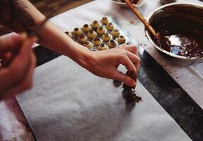 Confectioner sprinkling cocoa powder on a handmade truffle dipped in a melted chocolate mass photo