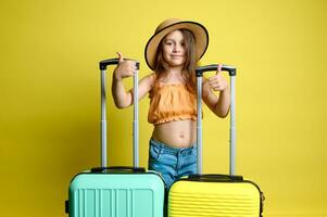 sonriente niño niña viajero pasajero pulgar arriba, en pie con amarillo y ligero verde policarbonato valijas foto
