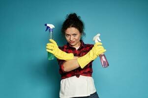 Young tired exhausted disgruntled housewife crossed her arms in denial, with cleaning sprays in hands photo