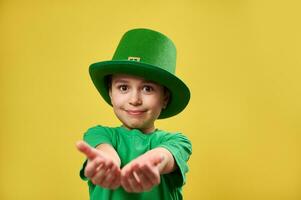 Boy in leprechaun Irish hat stretches his palms to the camera. Saint Patrick's Day concept. Copy space and yellow background photo