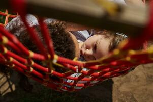 adorable pequeño niña besos su madre, acostado siguiente a su y relajante en un hamaca en un calentar soleado día foto