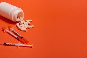 Composition with insulin syringes and pharmaceutical pills scattered from white medicament container on orange background with copy space for medical ad for World Diabetes Awareness Day 14 November. photo