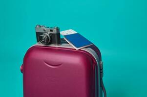 Close-up. Vintage camera and passport with ticket and boarding pass on a suitcase luggage, isolated over blue background with copy ad space photo