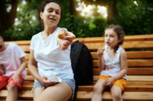 Focus on a dried figs fruit in the hands of a smiling woman, cheerful mother chilling out with her kids in the city park photo