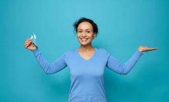 Smiling mixed race beautiful woman wearing blue casual clothes, holds a blue awareness ribbon and puts palm up holding imaginary copy space for medical advertising for World Diabetes Day, 14 November photo