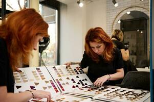 Focus on a mirror reflection of a redhead professional female hair stylist looking at palette of hair dye samples and choosing color of hair dye photo