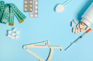 World Diabetes Awareness Day. White refined sugar, caliper, measuring tape, scattered pills, blister with medicines and insulin syringe with copy space at center on blue colored background. Flat lay photo