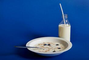 Closeup composition of fresh milk and a plate of muesli with berries, isolated on blue background photo