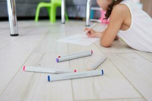 Focus on felt-tip-pens or watercolor markers on the floor on the background of blur little girl, drawing picture at home photo