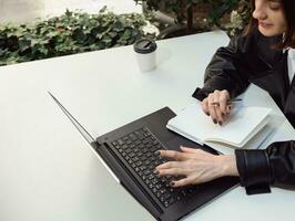 Overhead view of concentrated woman, business person, journalist, freelancer, copywriter, writing texts on notepad, typing on keyboard of a laptop computer. Online remote work and freelance concept photo