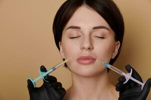 Close-up portrait of a beautiful young brunette receiving beauty injections on her face. Hands in black medical gloves holding syringes with hyaluronic acid product and giving anti-aging treatment photo