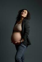 Studio portrait of a delightful gorgeous pregnant woman holding her belly, isolated gray background. Beautiful pregnancy photo