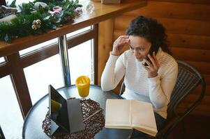 Young woman working online at a cafe, talking on mobile phone and looking at a tablet on a table photo