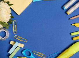 Flat lay composition of an assortment of school office accessories in yellow shades, isolated on blue background, copy space. Aster flower and stationery supplies scattered in a circle. Top view. photo