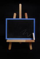 Close-up studio shot of a wooden table easel with a chalk and blackboard with empty blank space for text, isolated on black background photo