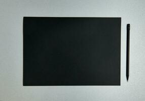 Flat lay composition of black sheet of design paper and black wooden pencil on a gray background. Top view photo