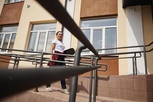View through the railing in the foreground to a beautiful woman holding a skateboard and going down the steps photo