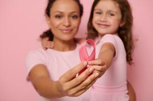 atención en rosado satín cinta en el manos de dos generaciones de mujer, madre y hija posando en rosado fondo, demostración apoyo, solidaridad a pacientes cáncer sobrevivientes mundo día de lucha cáncer foto