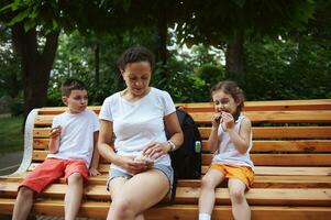 Authentic happy mother and her cute kids, son and daughter chilling out outdoors, enjoying a family walk on summer day photo