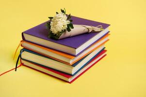 Beautiful bouquet of autumn asters flowers in craft wrapping paper tied in rope lying on stacked multicolored books. Teacher's Day concept, literary, knowledge, education. Yellow background copy space photo