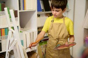 Adorable teen boy, 11 years schoolboy enjoys his hobby, drawing on canvas in an art workshop. Kids artistic development photo