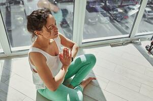 alto ángulo ver de un atractivo mujer ejecutando padmasana, inhalando aire y haciendo respiración ejercicios durante yoga práctica a hogar foto