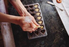 Top view of squeezing filling of salted caramel cream from confectionery bag into candy molds for preparing handmade chocolate pralines photo