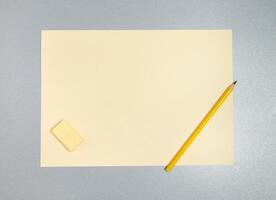 Flat lay photo of yellow eraser, pencil and sheet of paper on a gray surface