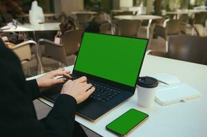 Rear view of female hands typing on laptop keyboard with green chroma key screen for ads. Mobile phone with green screen and copy space. Business, freelance, copywriting, online remote work concept photo