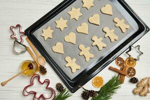 Top view of laid out gingerbread cookies on pastry rack. Cookies cutter, honey, pine scones and branches, dried slices of orange on wooden surface. Cooking process. Christmas preparations. 25 December photo