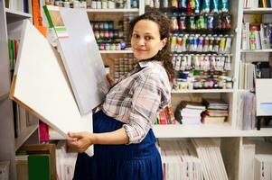 Beautiful pregnant woman artist, painter holding canvases, smiling looking at camera standing in a creative art store photo