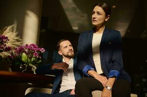 Portrait of two confident people, colleagues on business trip, Caucasian woman and man , business partners sitting on armchair in the lounge zone of a luxury hotel photo