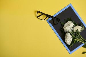 Flat lay of delicate beautiful bouquet of asters autumn flowers and glasses on a blank empty chalkboard with space for text isolated on yellow background photo