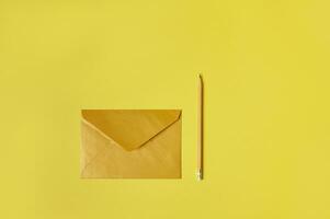 Flat lay composition of a yellow or golden envelope near a yellow wooden pencil isolated on a yellow background. Copy space photo