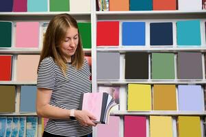 Confident young woman, seller in a school stationery store, holding a stack of blank copybooks with copy ad space photo