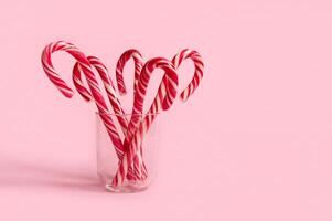 Beautiful minimalistic simple composition with Christmas lollipops on transparent glass on pink colored background with copy space for christmas ad photo