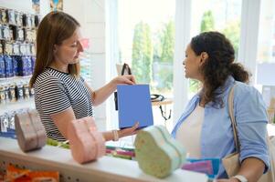 Pleasant Caucasian saleswoman showing color paper bags for gifts to a pregnant woman, shopping in creative art store. photo