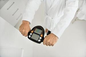 Top view of male hands holding the handle of a smart scale. Close-up of a mature man's hand in a white terry bathrobe weighing on a medically smart scale to determine the biological age and vitality photo