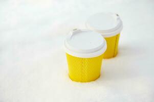 Two yellow takeaway paper cups with hot drink on a white fluffy snow in the winter park photo