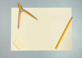 parte superior ver de amarillo herramientas para dibujo. lápiz, Brújula, borrador y sábana de papel en un gris superficie foto