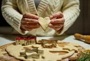 Close up of chef's hands holding heart shaped cut out gingerbread dough while making Christmas cookies photo
