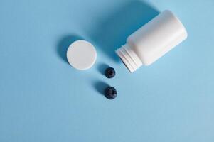 Flat lay composition of blueberries scattered from an opened white container on blue background photo