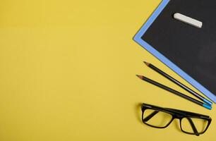 Flat lay composition. Chalk on a clean blackboard with copy space , eyeglasses and two pencils, isolated on yellow background with space for text photo