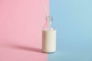 Studio shot of bottle with fresh milk with straw on bicolor pink and blue background. photo