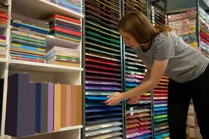 Caucasian female sales manager arranges multi colored cardboard paper sheets on retail shelves in a creative art store photo