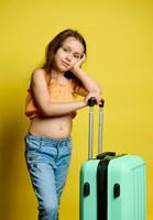 Authentic studio portrait of a cute little girl in summer wear, with light green valise, looking at camera. Air flight photo