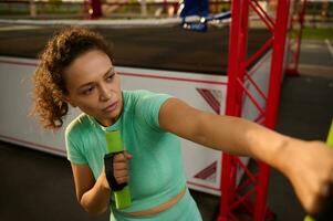 de cerca de un hermosa determinado deportivo mujer en movimiento, hacer ejercicio en el campo deportivo, boxeo con pequeño mancuernas, ejecutando un cardio rutina de ejercicio foto