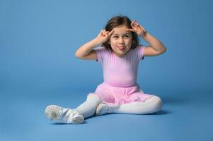 aislado retrato terminado azul antecedentes de un adorable preescolar niña bailarina haciendo muecas y demostración su lengua . foto