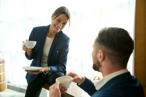 Attractive young woman in business suit sitting at table in hotel room and smiles sweetly talking with her boss or business partner over a cup of coffee. Partners relationships and closeness at work photo