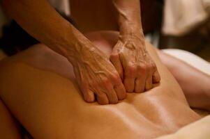 Ayurvedic treatment, professional therapeutic body massage at the wellness spa complex. Close-up. Young man relaxes while lying on a massage table during a therapeutic back massage at a luxury spa. photo